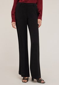 Zwarte wijde broek met een gladde stofafwerking, met een standaard taille en subtiele plooien. Gecombineerd met een bordeauxblouse.