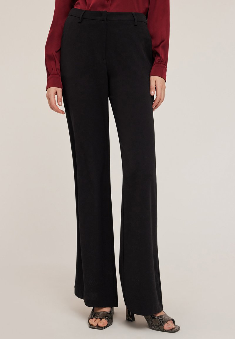 Zwarte wijde broek met een gladde stofafwerking, met een standaard taille en subtiele plooien. Gecombineerd met een bordeauxblouse.