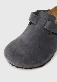 Γκρι μοκασίνι από σουέντ με φαρδύ στρογγυλεμένο δάχτυλο και λουράκι στο πάνω μέρος, εμφανίζεται σε λευκό φόντο.