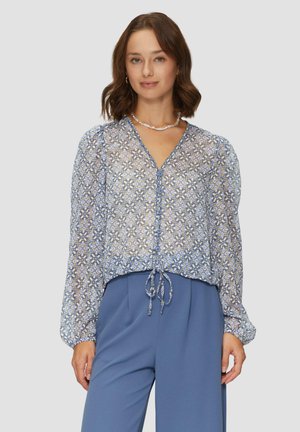 Blouse florale bleue transparente à manches longues bouffantes, avec un devant à boutons et un ourlet à cordon. Associée à un pantalon bleu clair.