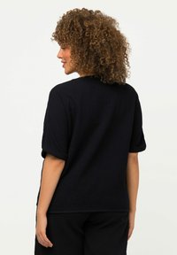 Camicia nera a maniche corte con texture, dal taglio rilassato e con risvolti, caratterizzata da un semplice scollo a girocollo e un leggero fondo allungato.
