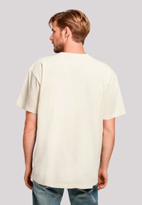 Hellbeige oversized T-Shirt mit kurzen Ärmeln und rundem Halsausschnitt. Glatte Stoffoberfläche und lässige Passform, von hinten betrachtet.