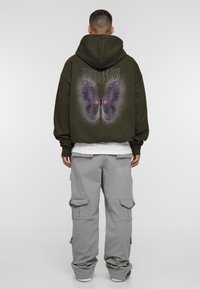 Olive green hoodie with a large butterfly graphic and logo on the back. Paired with grey cargo pants featuring multiple pockets.