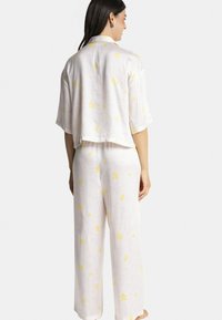 Ensemble de pyjama avec motif floral en tissu doux et léger. Comprend un haut court à manches courtes et un pantalon à larges jambes en rose pastel avec des accents jaunes.