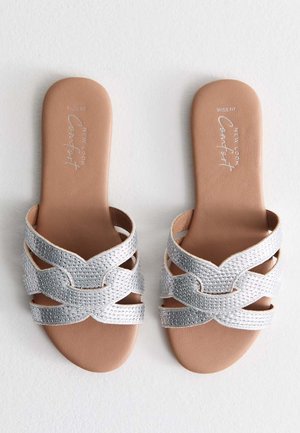 Sandali slip-on argento con vestibilità ampia; caratterizzati da cinturini incrociati decorati con piccole pietre di strass e una soletta liscia color bronzo.
