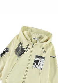 Felpa gialla con zip frontale, stampe grafiche nere, tra cui un coniglio e del testo. Presenta un piccolo patch con un design a onda. Tessuto morbido.