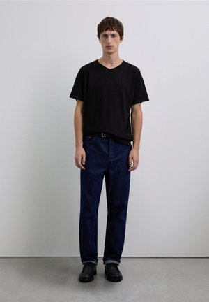 Zwart V-hals T-shirt met korte mouwen, gecombineerd met donkerblauwe rechte jeans en zwarte schoenen. Soepele stof met minimale ontwerpdetails.