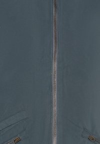 Let blå jakke med lynlås foran og to sidelommer med skrå låg. Glat tekstur med minimalistisk design.