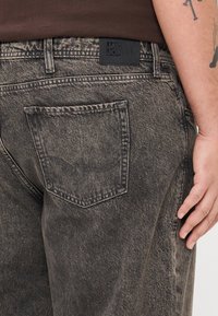 Blugi din denim gri închis cu o textură uzată, având o aplicație pe spate și o etichetă neagră la talie cu brandingul "Jack & Jones".