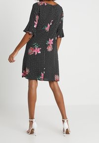 Mustavalkoinen pilkullinen mekko, jossa on vaaleanpunaisia ja vihreitä kukkaelementtejä. Mekossa on lyhyet kellohihat ja takana napitus. Mekkoa on yhdistetty valkoisiin korkokenkiin.