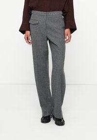 Pantalones de lana gris con pierna recta, bolsillo delantero y pasadores para cinturón. Textura suave y un ajuste entallado, combinados con mocasines negros.