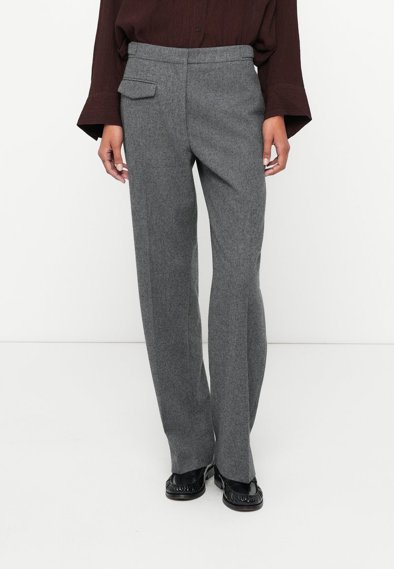 Pantalones de lana gris con pierna recta, bolsillo delantero y pasadores para cinturón. Textura suave y un ajuste entallado, combinados con mocasines negros.