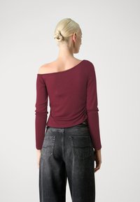 Maglietta bordeaux a maniche lunghe con design off-shoulder, abbinata a jeans grigi scuri a vita alta con tasche posteriori e vestibilità comoda.