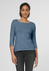 Blauer Strickpullover mit Rundhalsausschnitt und Dreiviertelärmeln. Glatte Textur und taillierte Passform, kombiniert mit dunkelgrauen Jeans.