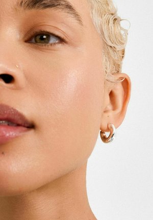 Silver hoop earring with a twisted design, featuring a reflective surface. Smooth texture and shiny finish, worn on an ear. Close-up view.