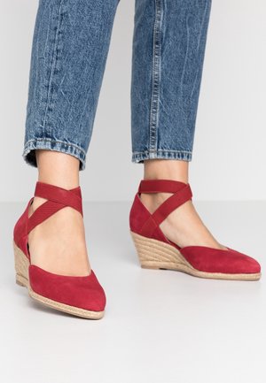 Czerwone zamszowe buty na koturnie z krzyżującymi się paskami na kostce i obcasem owiniętym jutą. Okrągły czubek i gładka faktura.