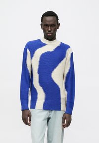 Suéter de punto en azul y crema con patrones ondulados, cuello alto y puños acanalados, complementado con un ajuste relajado.