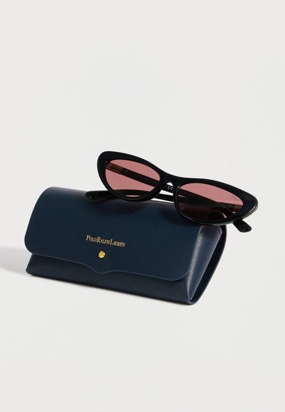Μαύρα γυαλιά ηλίου cat-eye με ροζ φακούς που ακουμπούν σε θήκη από ναυτικό μπλε δέρμα Polo Ralph Lauren με χρυσά γράμματα και κούμπωμα με κουμπί.