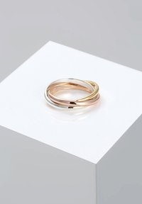 Drie in elkaar grijpende ringen van goud, roségoud en zilver. Gladde, gepolijste oppervlakte met afgeronde randen, tentoongesteld op een wit voetstuk.