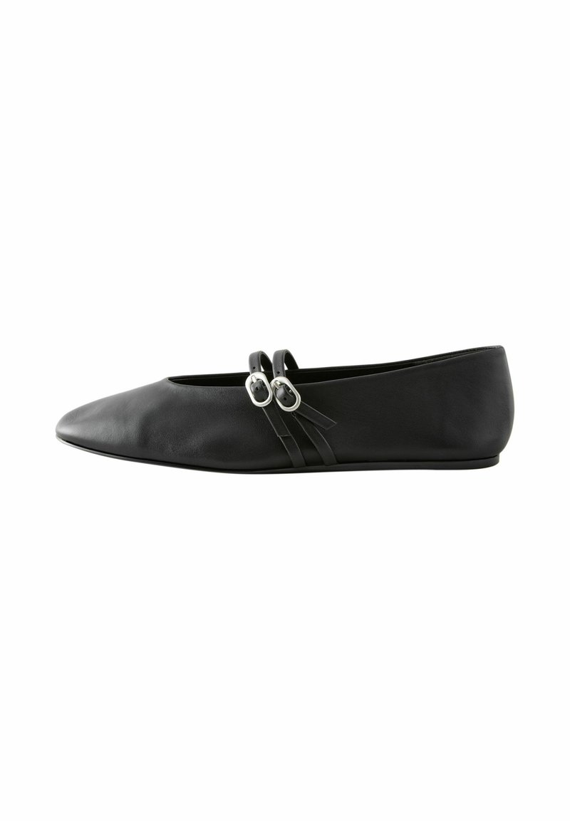 Chaussure plate noire avec bout pointu et deux fines brides croisées avec boucles argentées sur le côté.