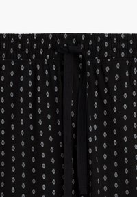 Czarne szorty dresowe z elastycznym paskiem w talii i sznurkiem, z powtarzającym się szarym wzorem zegarów na miękkim materiale.