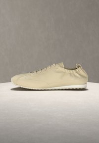 Μπεζ δερμάτινο αθλητικό παπούτσι με λευκή οδοντωτή σόλα, ελαστικό κολάρο αστραγάλου, μπροστινό δέσιμο με κορδόνια και θηλιά στο πίσω μέρος, πάνω σε ουδέτερο φόντο.