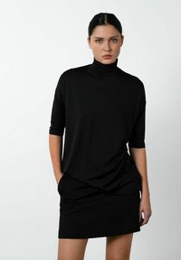Sort strækstofkjole med høj turtleneck, trekvartærmer og en afslappet pasform, der har en glat tekstur og ingen synlige mønstre.