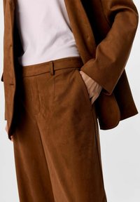 Brun ruskindsdragt med vidde bukser og en matchende blazer; glat tekstur med lommer og en tætsiddende overdel under.
