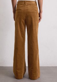 Bruine corduroy wijde broek met een gestructureerde afwerking, voorzien van twee achterzakken en een nette zoom.