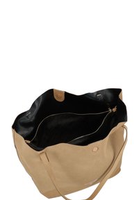 Bolso tote de ante beige con interior negro, que cuenta con asas dobles, un compartimento con cremallera y un logo de la marca visible en el exterior.