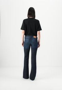 Black short-sleeve t-shirt paired with dark blue flared jeans featuring a branded leather patch and distinct back pocket stitching.