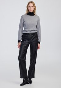 Pull gris à manches longues avec un col roulé noir, associé à un pantalon en cuir noir taille haute et des bottes à talons noires.
