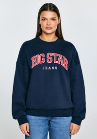 Tmavě modrá mikina s kulatým výstřihem, spadlými rameny a žebrovanými manžetami. Na přední straně velký nápis "BIG STAR JEANS" v červené a bílé barvě.
