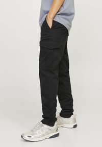 Pantalones cargo negros con un ajuste slim, que cuentan con bolsillos laterales y una textura de algodón suave, combinados con zapatos deportivos de color claro.