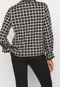 Schwarz-weiße Bluse mit Karomuster, langen Ärmeln und Rüschensäumen, runder Ausschnitt und sanfter Textur.