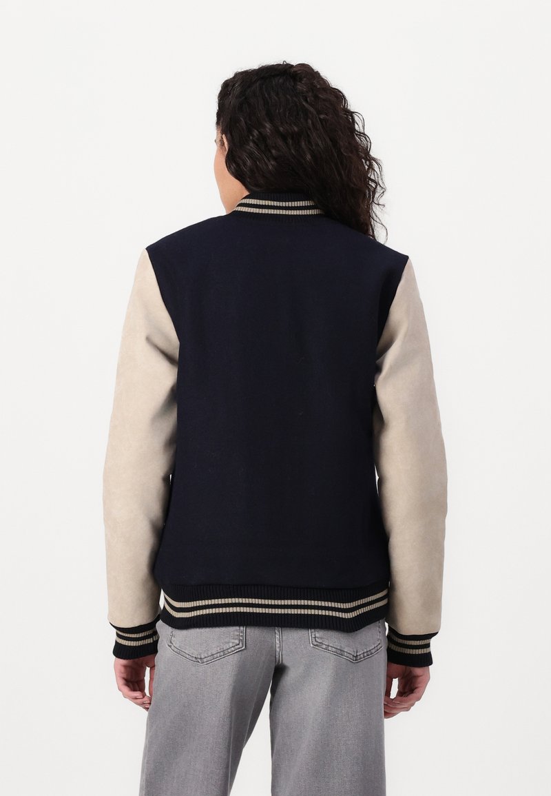 Marineblaue Collegejacke mit beigefarbenen Wildledermanschetten, geripptem Kragen und Bündchen, die cremefarbene und schwarze Streifen aufweisen, sowie einem taillierten Saum.