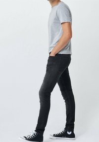 Camisa de manga corta gris, jeans skinny negros y zapatillas negras de caña alta. Los jeans tienen bolsillos laterales y un sutil detalle de logo.