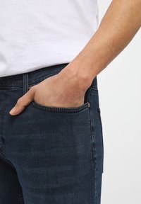 Tamsiai mėlynai džinsai su tvirtu dizainu. Audinys turi lengvą tekstūrą, o kišenėje yra auksinė mygtuko detalė.