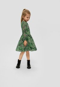 Grünes Blumenkleid mit langen Ärmeln, gerafftem Rock und schwarzen Kampfschuhen. Verfügt über eine durchsichtige Überlagerung mit rosa und lila Akzenten.