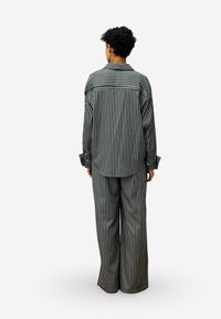 Striped pajama set featuring a collared shirt with button cuffs and wide-leg pants. Colors include black and white in vertical stripes.