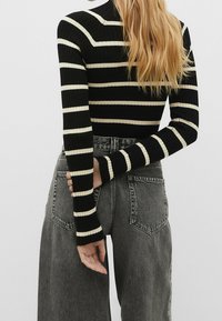 Haut rayé noir et crème à côtes, à manches longues et col montant, associé à un jean taille haute gris avec poches.