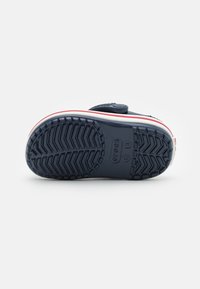 Semelle de sneaker marine avec un motif de bande de caoutchouc texturé, agrémentée d'une rayure blanche et rouge sur le côté. Fermeture Velcro sur le dessus.