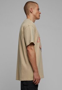 Bēša kokvilnas T-krekls ar īsām piedurknēm, ar apdrukātu dizainu sarkanā un melnā krāsā. Piegriezums ir brīvs, ar taisnu apakšmalu.