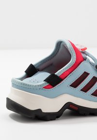 Vaaleansiniset tennarit, joissa on vaaleanpunaiset verkkoaksentit, mustat hihnat ja teksturoitu kumipohja. Ominaisuuksiin kuuluvat rei'itys ja pehmustettu kaulus mukavuutta varten.