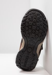 Svart gummisul med cirkulära mönster, förstärkta kanter och Geox-logotyp; har en grå mellansula och en strukturerad yta för bra grepp.
