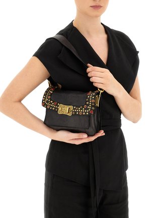 Borsa a tracolla in pelle nera con borchie decorative in rosso e oro. Ha una forma strutturata, un gancio frontale e una tracolla removibile.