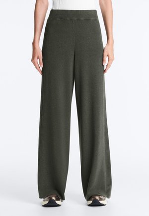 Ciemnozielone dzianinowe spodnie o szerokich nogawkach z prążkowymi bokami, noszone z białą bluzką i trampkami, pokazane od pasa do stóp na neutralnym tle.