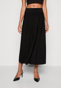 Gonna nera plissè con ampio elastico in vita, design fluido e tessuto leggero, abbinata a tacchi a punta neri.