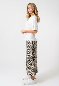 Top bianco smock con maniche corte, abbinato a una maxi gonna leopardata chiara e sneakers bianche chunky.