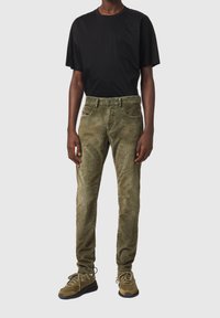 Pantalones de pana verde oliva con corte recto, combinados con una camiseta negra de manga corta y zapatillas verde oliva. Diseño sencillo, costuras visibles.